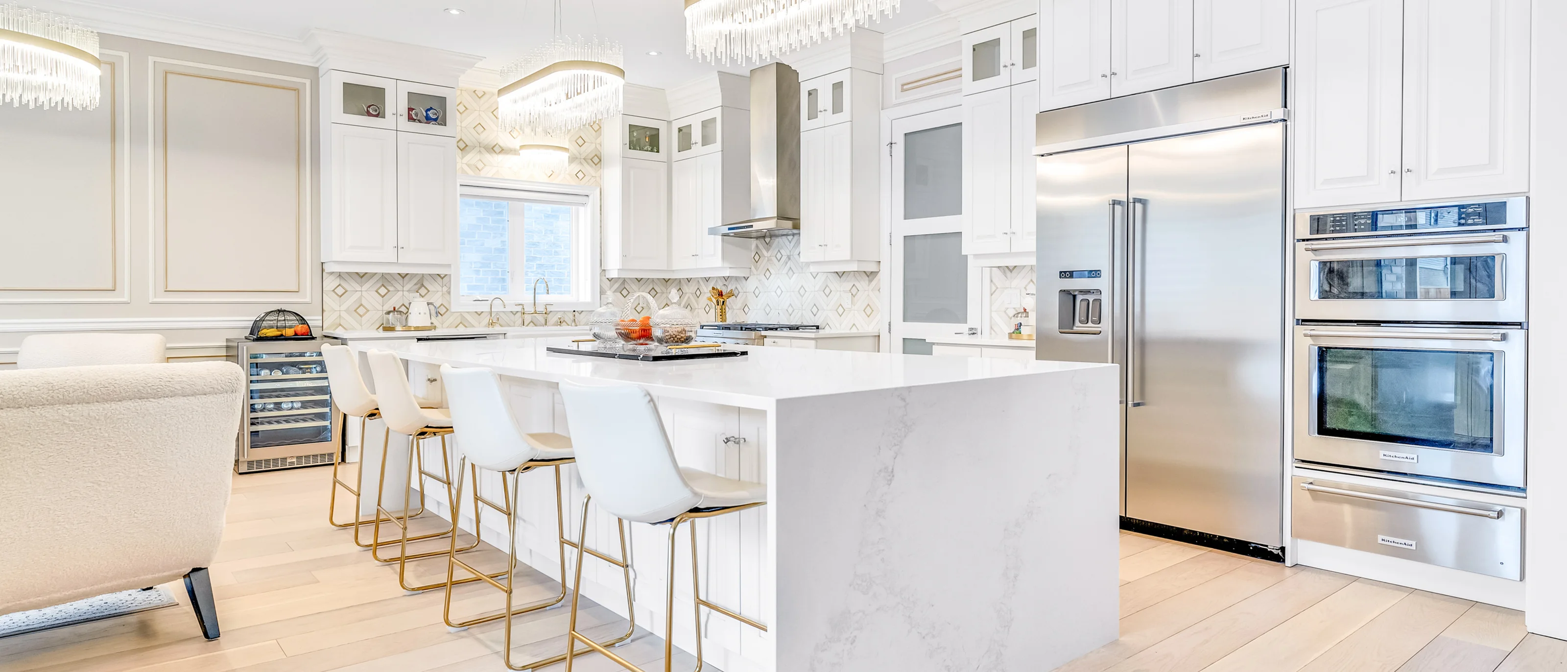 White kitchen with a marble waterfall island and gold bar stools